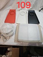 Three Geni Ware snack trays in red, white, and black, stacked napkins, and vintage Tupperware egg carrying tray with lid displayed flat on white cloth