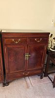 Front view of antique hardwood cabinet, showing two upper drawers, two front doors with brass latch, and lower drawer, all on carved claw feet.