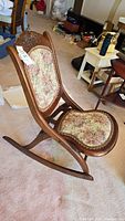 Side view of antique solid wood folding rocking chair showing carved details and floral upholstery.