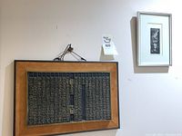 View of two framed Asian art pieces hanging on wall, showing both large script relief and smaller floral print.