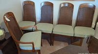 Five wooden chairs with cane backs and striped seat cushions, one with armrests