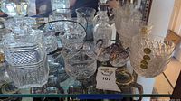 Various glass kitchenware including decanters, glasses, bowls, and decorative pieces on a mirrored surface.