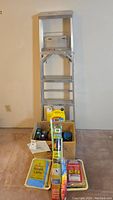 Photo of aluminum step ladder with cleaning supplies placed in front in boxes and bags