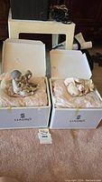 Two Lladro figurines on their respective white Lladro branded boxes, wrapped in tissue paper, placed on carpet.