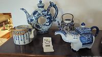 Four blue painted porcelain tea pots lined up, showing variety of designs including dragon, floral, elephant, and calligraphy.