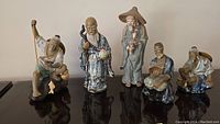 Wide photo of all five Shekwan porcelain figurines showing various poses and objects including a large peach, staffs, fishing pole, fan, and gourd