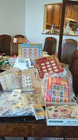 Photo showing multiple stamp sheets, loose stamps, and partial envelopes on a dining table.