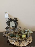 Photo showing the stone fruit bowl containing assorted stone fruit with a small ornate mirror behind on a lace doily on a wooden surface.