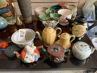 Seven items displayed on glass table, all teapots in front and vase at rear left