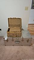 Large metal steamer trunk with three wicker picnic baskets stacked on top, showing the overall size and structure