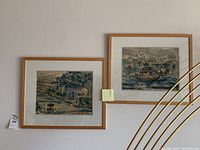 Two framed watercolor landscape paintings by Wendy Yeo hanging on a wall. Light wooden frames with white matting.
