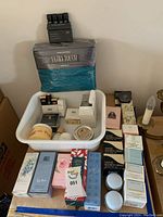 Photo displaying boxed perfumes, lotions, and other beauty items arranged on a table including Elizabeth Arden and Enrico Coveri products alongside a body cream and other treatments.
