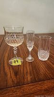 Three different types of glasses displayed on wooden table: red wine glass with wide bowl, a slender sherry glass, and a cylindrical water glass, all with cut crystal designs.