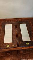 Two identical stained wood framed rectangular mirrors placed side by side on a wood surface showing the front view.