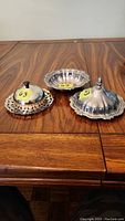 Three silver plated dishes displayed on wooden table; two with lids and one open dish with scalloped edge