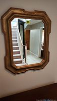 Full view of the antique gold painted framed mirror hung on a wall showing the shape and size in a home setting.