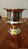 Front view of silver plated champagne bucket showing two decorative handles and pedestal base.