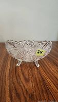 Clear lead crystal bowl with scalloped edges and three legs, showing detailed cut patterns on the side, placed on a wooden surface.