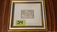 Framed silver plated print showing the overall item with white and gold wood frame and glass, with a label 34.