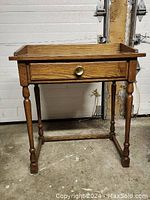 Front view of small wood desk showing hand-turned legs and central drawer with brass knob.