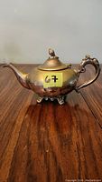 Front left side view of vintage teapot showing curved spout, ornate handle, and decorative feet