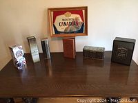 Wide view of all eight items including Molson Canadian plaque and seven assorted collector cans on table.
