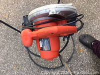 Top view of the orange Black and Decker circular saw with black power cord coiled around it on an outdoor surface.