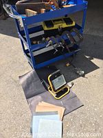 Blue metal roller cart loaded with assorted hand tools and a toolbox on a sunny concrete surface