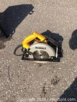 Photo of the DeWalt circular saw showing the yellow handle, blade guard, and metal blade placed on asphalt surface.