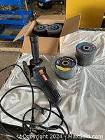 Electric angle grinder in front, multiple stacks of flap discs behind