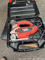 Red and black Black & Decker jigsaw in open molded black plastic carrying case with power cord coiled inside case.