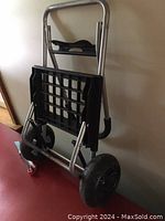 Photo showing the front view of the light 2 wheel folding dolly leaning against a wall, highlighting the metal frame, black plastic platform, handle and wheels.
