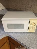 Full view of Kenmore small white microwave oven on countertop, showing the front door with glass window and control panel with timer dial.