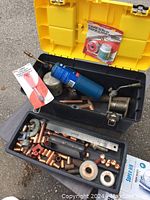 Photo showing yellow plastic toolbox open with assorted copper pipe fittings, rolls of solder and flux, propane torch cylinder, pipe cutter, and other plumbing tools.
