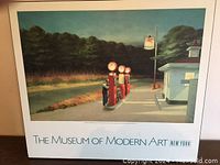 Full view of the large print showing the gas pumps, man, building and sign under night sky