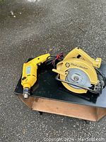 Photo showing the Black & Decker circular saw and a yellow hammer drill on a black surface outdoors.