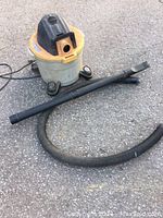 Full view of shop vac showing motor unit, canister base, and hose plus wand attachments on pavement.