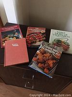 Five cookbooks laid out on a dark wood surface showing titles and covers
