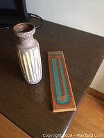 Photo of a ceramic vase alongside a wooden cribbage board on a dark wooden surface.
