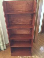 Wooden bookcase seen from front, showing all five shelves and wood grain finish.