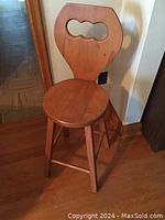 Wooden stool with round seat and solid backrest featuring a central decorative cutout. Stool has four tapering legs connected with a horizontal footrest bar.