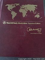 Front cover of Rand McNally World Atlas Signature Edition with embossed gold world map and signature.
