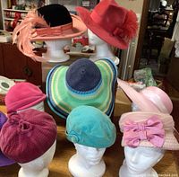 Nine hats on display including felt brimmed hats with feathers, velvet cloche hats, a multicolor straw sun hat, and velvet caps in pink, purple, and turquoise.