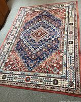 Full view of the rectangular area rug showing the central blue diamond medallion and surrounding rust-red field with floral motifs, and cream-colored borders with geometric patterns.