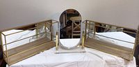 Two new mirrored display shelves with gold metal trim and wooden bases alongside a tall oval vanity mirror with an acrylic stand, all placed on a white cloth.