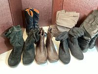 Photo showing six pairs of boots including men's cowboy boots and multiple women's boots varied in height and materials.