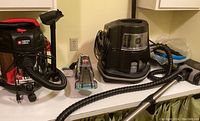 Photo showing the Porter Cable shop vac, Bissell stain remover, and Rainbow vacuum with attachments arranged on a white surface.