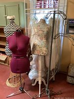 Four dress forms and a metal clothing rack displayed indoors with various background items.