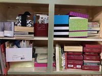Shelf filled with various boxes of greeting cards and stationary, including floral patterned boxes, metallic tins, and assorted paper products.