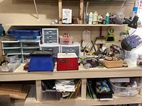 Wooden bench with multiple small plastic drawer units holding stained glass pieces, assorted tools and accessories on shelf and surface